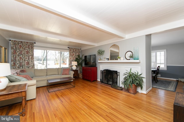 living area featuring baseboards, beamed ceiling, light wood-type flooring, and a brick fireplace