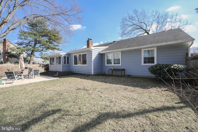 rear view of house featuring a shingled roof, fence, a lawn, a chimney, and a patio area