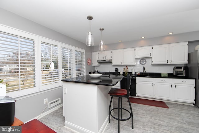 kitchen featuring dark countertops, light wood-style flooring, white cabinetry, a sink, and under cabinet range hood