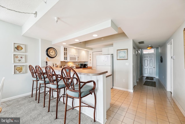 kitchen with a peninsula, white appliances, white cabinetry, a kitchen bar, and glass insert cabinets