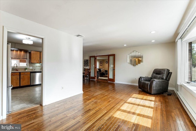 unfurnished room featuring a baseboard heating unit, visible vents, a sink, and wood finished floors