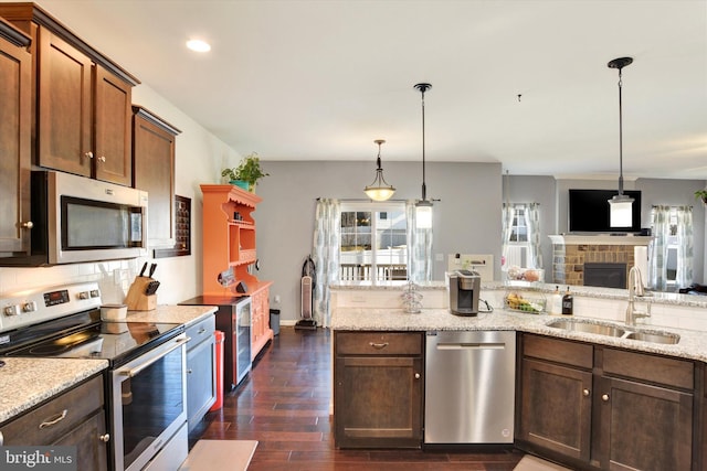 kitchen with hanging light fixtures, light stone counters, stainless steel appliances, and a sink