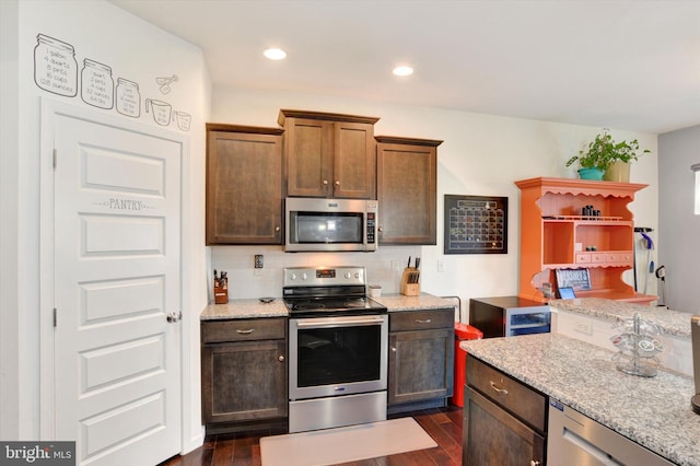 kitchen with appliances with stainless steel finishes, dark wood-type flooring, and light stone counters