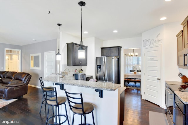 kitchen featuring appliances with stainless steel finishes, open floor plan, light stone counters, a peninsula, and pendant lighting