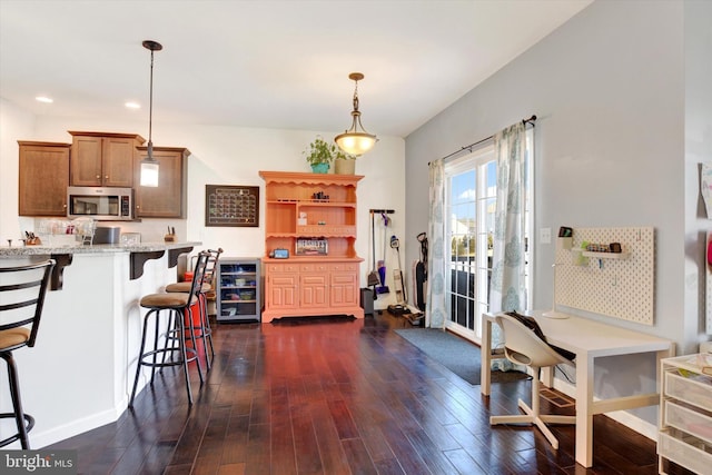 kitchen with dark wood-style floors, wine cooler, stainless steel microwave, light stone countertops, and pendant lighting