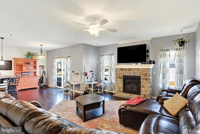 living area with a ceiling fan, dark wood finished floors, a stone fireplace, and baseboards