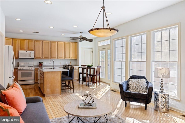 kitchen with decorative light fixtures, white appliances, open floor plan, light countertops, and a center island with sink