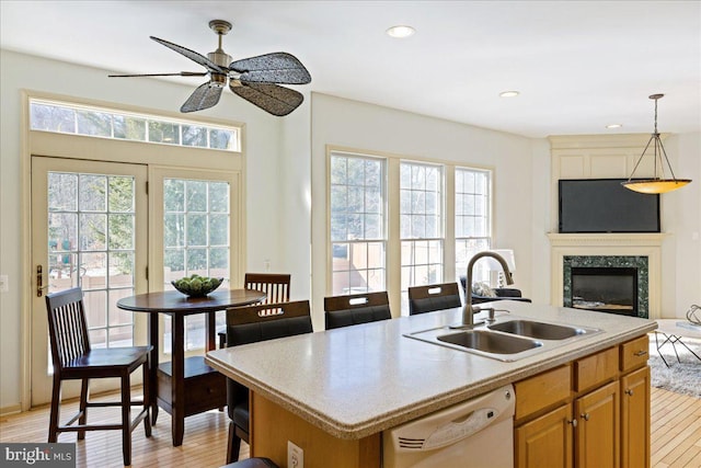 kitchen featuring light wood-style flooring, a sink, hanging light fixtures, dishwasher, and an island with sink