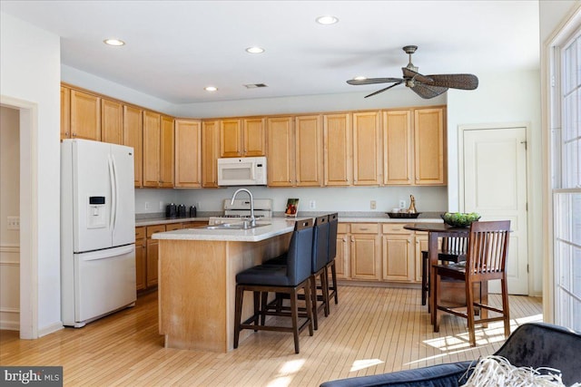 kitchen featuring light countertops, visible vents, a kitchen island with sink, white appliances, and a kitchen bar