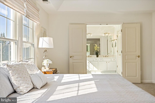 bedroom featuring ensuite bath, baseboards, a sink, and light colored carpet