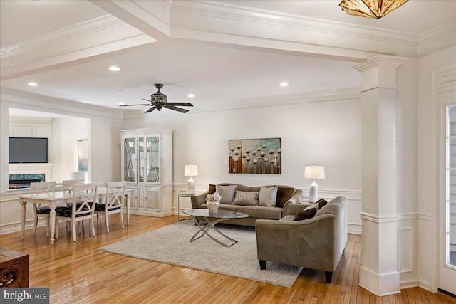 living room featuring a wainscoted wall, a fireplace, light wood-style floors, ornamental molding, and ornate columns