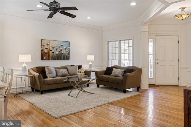 living area featuring a wainscoted wall, crown molding, a decorative wall, light wood-style floors, and ornate columns