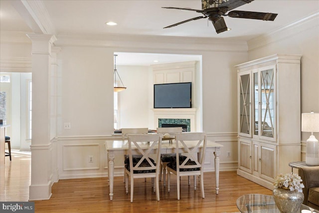 dining room featuring a high end fireplace, light wood-type flooring, decorative columns, and ceiling fan