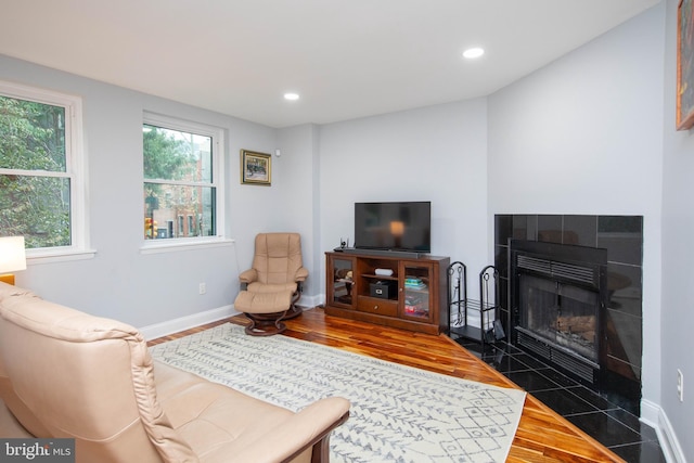 living room with dark wood-style floors, baseboards, a healthy amount of sunlight, and a tiled fireplace