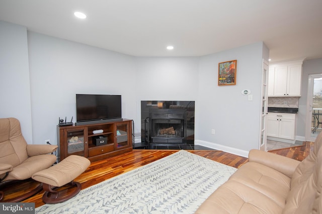 living area with recessed lighting, baseboards, a tiled fireplace, and wood finished floors