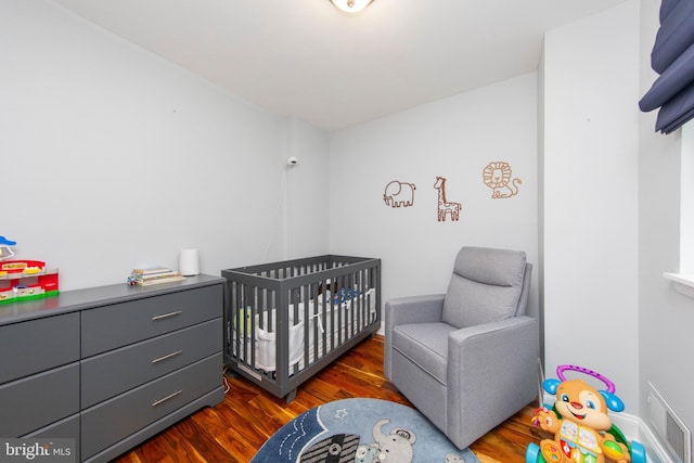 bedroom with a crib, dark wood finished floors, and visible vents