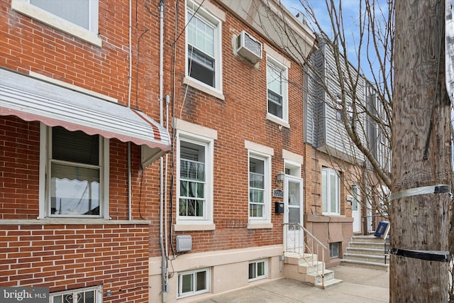 view of home's exterior with entry steps, brick siding, and a wall unit AC