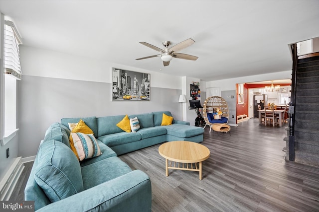 living area with ceiling fan with notable chandelier, wood finished floors, stairs, and baseboards