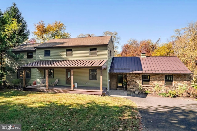 rear view of property featuring stone siding, a chimney, metal roof, a standing seam roof, and a yard