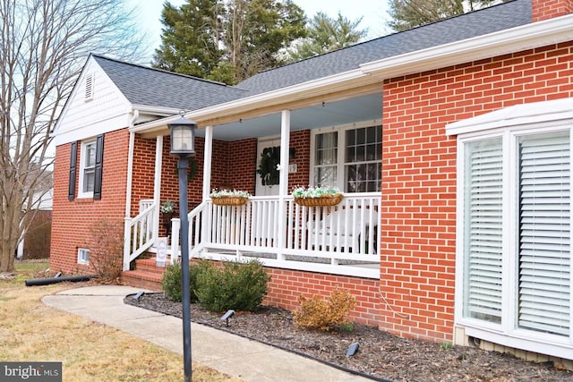 property entrance featuring covered porch, brick siding, and roof with shingles