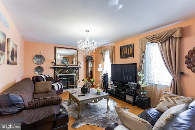 living area with visible vents, a chandelier, wood finished floors, and a glass covered fireplace