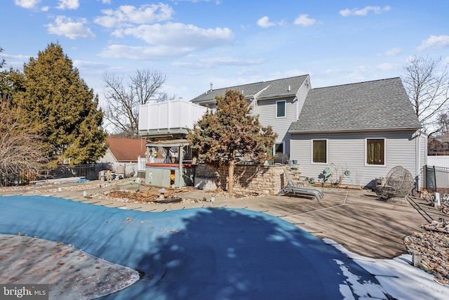 back of property featuring a hot tub, a shingled roof, fence, and a fenced in pool