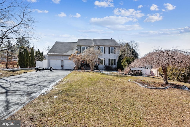 colonial-style house with aphalt driveway, a front yard, fence, and a garage