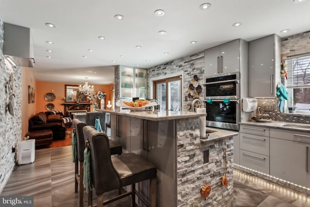 bar with a notable chandelier, tasteful backsplash, stainless steel double oven, and recessed lighting