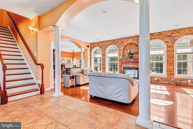 living room featuring light tile patterned floors, decorative columns, stairs, and a glass covered fireplace