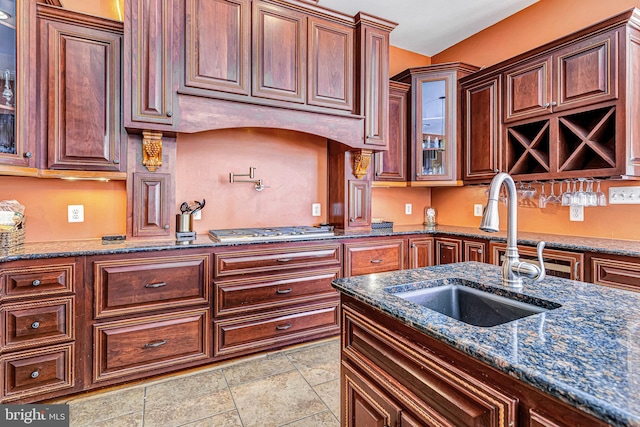 kitchen with stainless steel gas cooktop, dark stone countertops, glass insert cabinets, and a sink