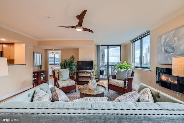 living room featuring ornamental molding, a glass covered fireplace, ceiling fan, and baseboards