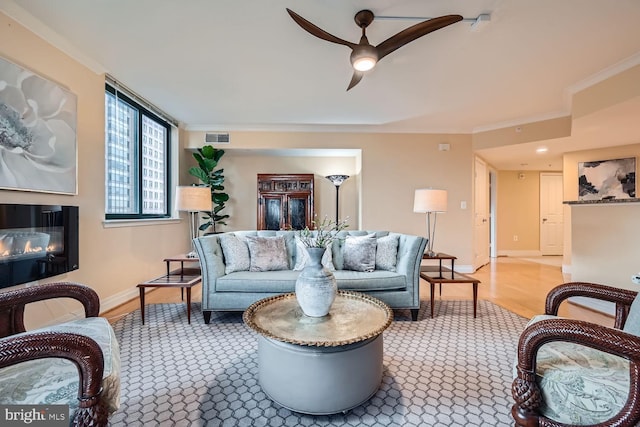 living room featuring wood finished floors, a glass covered fireplace, visible vents, and crown molding