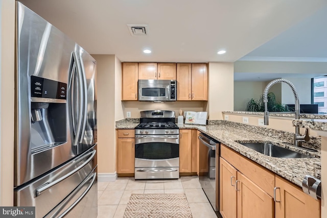 kitchen featuring visible vents, appliances with stainless steel finishes, light stone countertops, light brown cabinets, and a sink