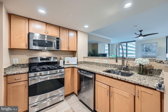 kitchen with light stone counters, light tile patterned floors, stainless steel appliances, light brown cabinetry, and a sink