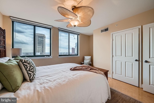 bedroom featuring a ceiling fan, multiple windows, visible vents, and wood finished floors