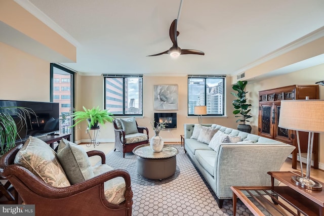 living area featuring ornamental molding, a glass covered fireplace, visible vents, and a ceiling fan