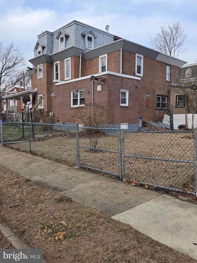 view of home's exterior with mansard roof, a fenced front yard, and brick siding