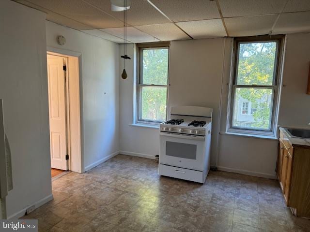 kitchen with baseboards, light countertops, a paneled ceiling, and white range with gas stovetop