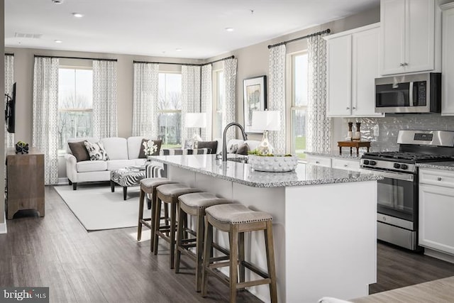 kitchen with white cabinetry, a kitchen breakfast bar, open floor plan, appliances with stainless steel finishes, and a center island with sink