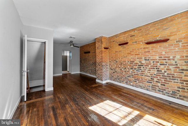 empty room with dark wood-style floors, visible vents, a ceiling fan, brick wall, and baseboards