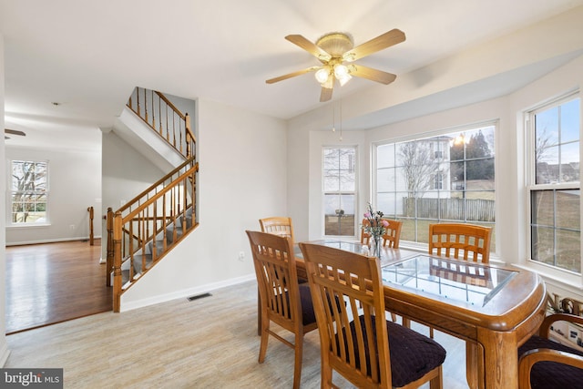 dining room featuring stairs, light wood finished floors, a wealth of natural light, and baseboards