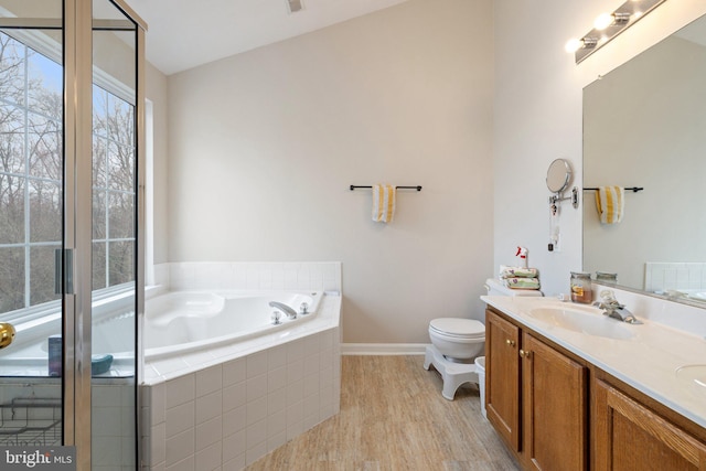 bathroom featuring toilet, wood finished floors, a sink, a bath, and double vanity