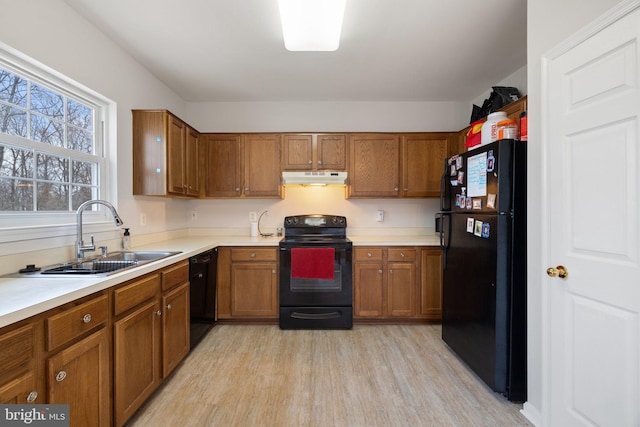 kitchen with brown cabinets, under cabinet range hood, light countertops, black appliances, and a sink