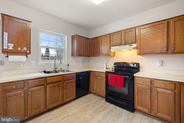 kitchen featuring brown cabinetry, a sink, under cabinet range hood, and black appliances