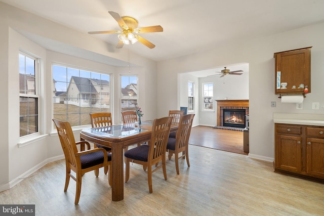 dining space with a ceiling fan, a brick fireplace, light wood-style flooring, and baseboards