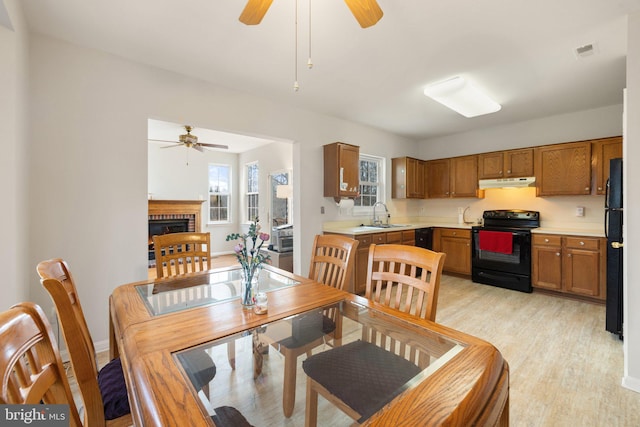 dining room with light wood finished floors, visible vents, a ceiling fan, a brick fireplace, and baseboards