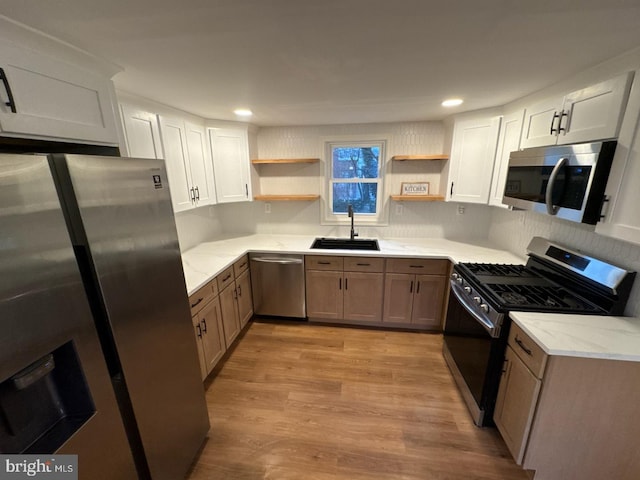 kitchen featuring appliances with stainless steel finishes, light stone countertops, light wood-style floors, open shelves, and a sink