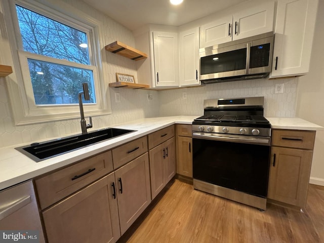 kitchen featuring stainless steel appliances, light countertops, light wood-type flooring, open shelves, and a sink