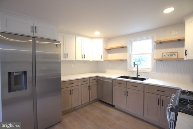 kitchen with appliances with stainless steel finishes, wood finished floors, light countertops, open shelves, and a sink