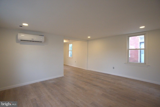 unfurnished room featuring a wall unit AC, baseboards, wood finished floors, and recessed lighting